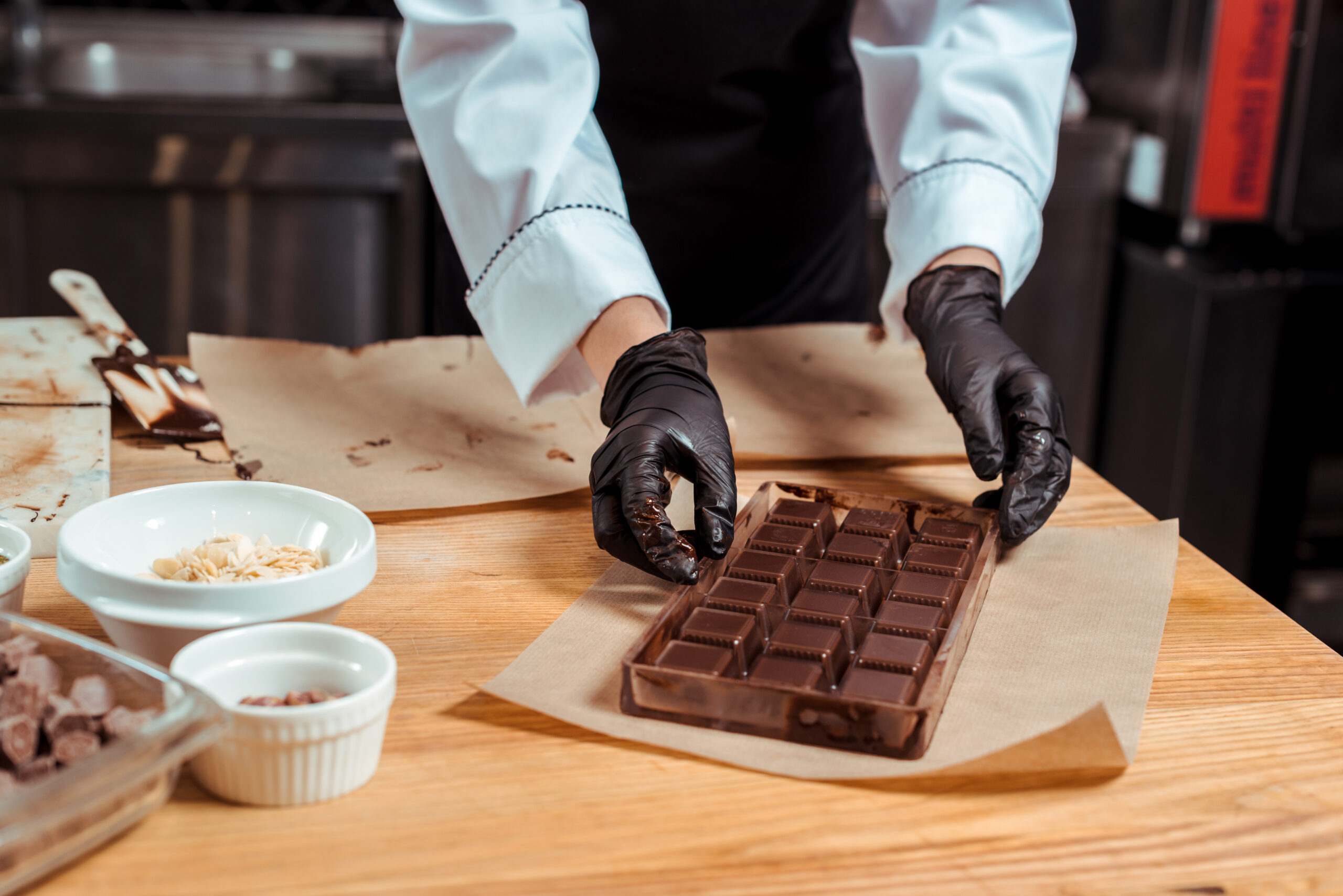 How to Start a Craft Chocolate Business cropped view of chocolatier holding chocolate molds with chocolate near baking paper