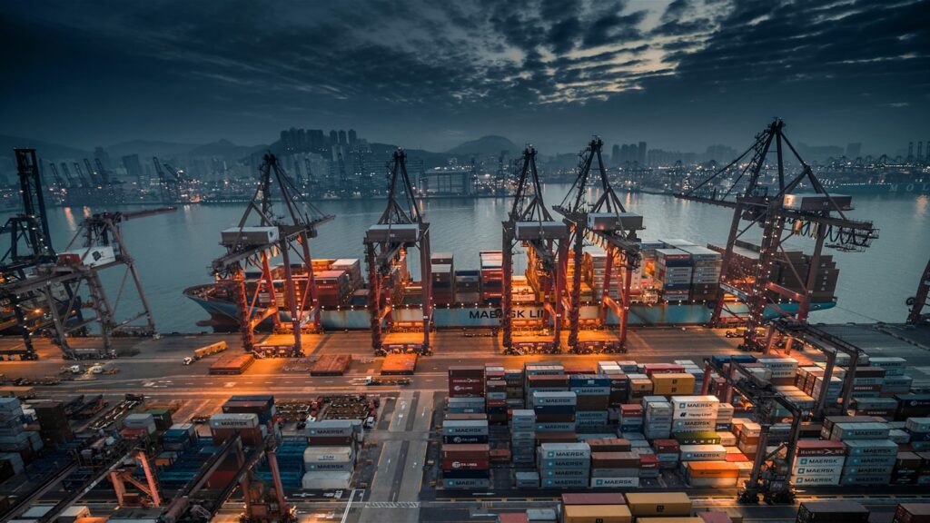 A container ship being loaded by cranes at an industrial port at dusk