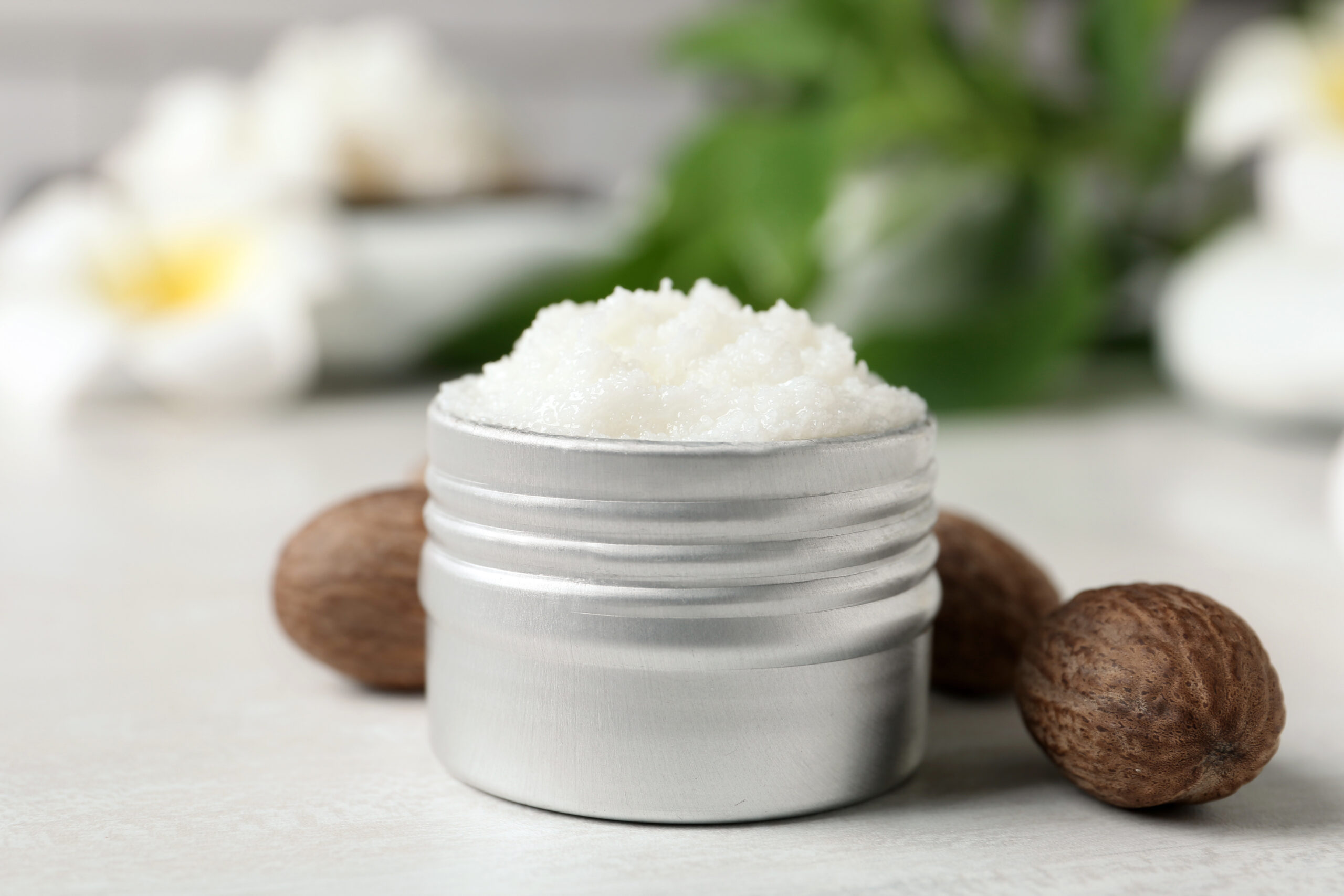Shea butter in jar and nuts on white table, closeup
